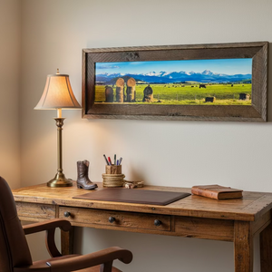 Framed panoramic landscape of a field with hay bales and mountains.