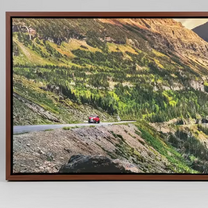 Framed photograph of a mountain landscape with a road and vehicle on a gray background