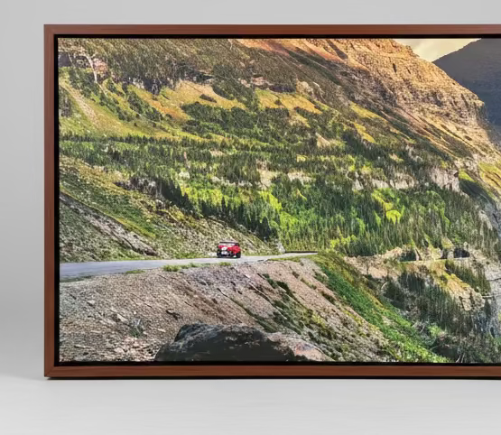 Framed photograph of a mountain landscape with a road and vehicle on a gray background